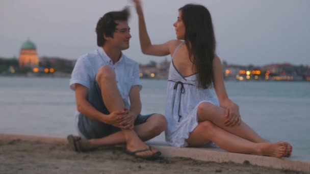 Beautiful young brunette caucasian girl takes care of her boyfriend hairstyle at the background of early morning summer venice water sunrise landscape — Stock Video