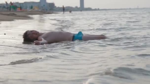 Kaukasische jongeman leggen op zand strand en plezier maken met water golven op roeping reis — Stockvideo