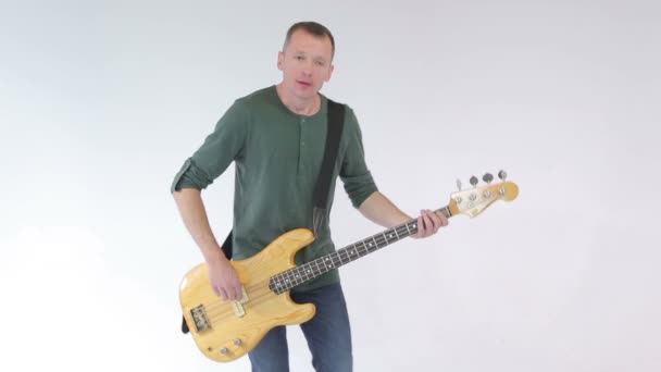 Bassgitarrist solo, spielt und springt zur Musik im tanzweißen Studiohintergrund — Stockvideo