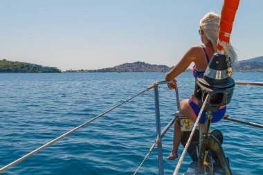 Yelkenli yat burun üzerinde oturan uzun sarı saçlı kız tekne ve seyir Poros Adası, Peloponnese, Yunanistan