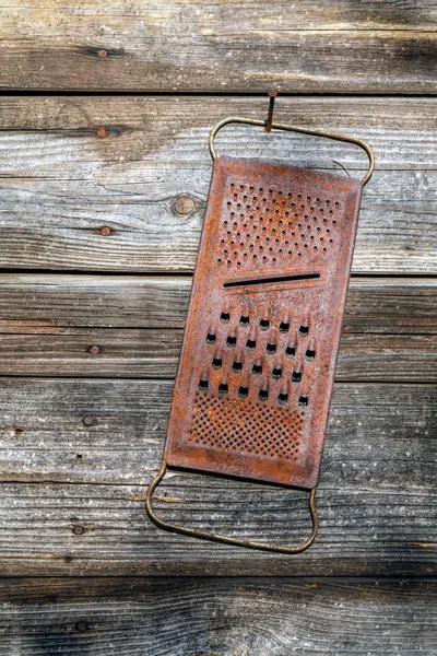 Rusty old kitchen grater hanging on the rusty nail on the background of wooden boards