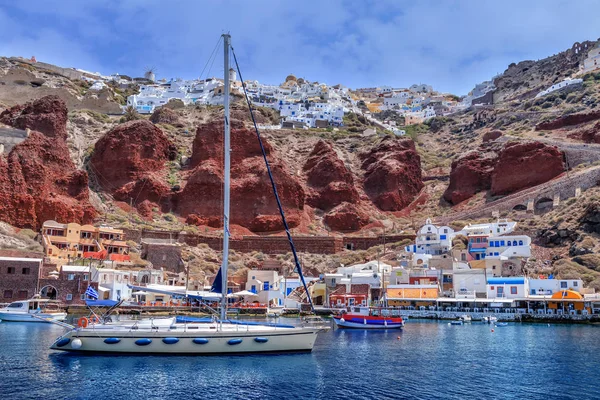Ιστιοπλοϊκό σκάφος και σκάφη κοντά το λιμάνι της Οίας, Σαντορίνη, Ελλάδα. Προβολή στο κόκκινο βράχοι Καλντέρα και λευκά σπίτια στον ουρανό — Φωτογραφία Αρχείου