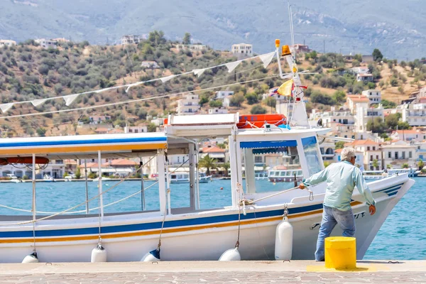 Πόρος, Ελλάδα - Αύγουστο 10,2016: άνθρωπος τραβάει το σκάφος στην ακτή για το σχοινί, αστικό τοπίο φόντου στην Πελοπόννησο — Φωτογραφία Αρχείου