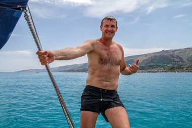 Yakışıklı mutlu adam yapma shaka tabelada yelkenli, lüks deniz gevşeme zevk gezisi. Yatçılık spor aktiviteleri ve yelken