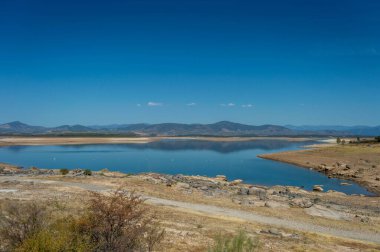 İklim değişikliğinden etkilenen göl mavi gökyüzü ile çevrili bir yaz gününde dağlarla çevrili.