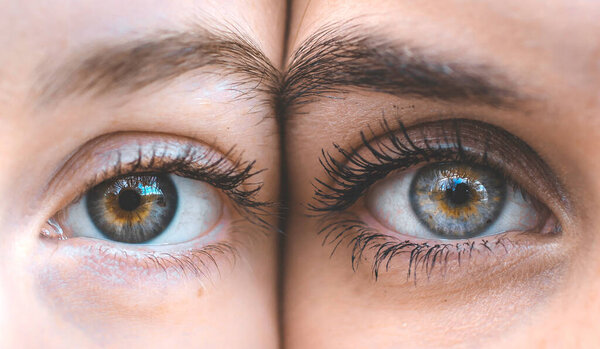 Closeup of beautiful green and blue eyes of two makeup girls looking at the camera
