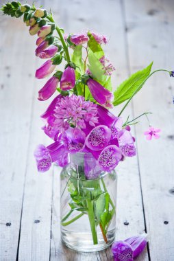 Gri ahşap arka planda, cam vazoda mor çiçekler.
