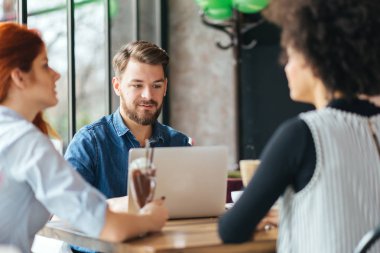 Kafede bir dizüstü bilgisayar kullanan genç gülümseyen adam.