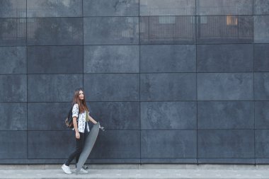 Modern binanın duvarının yakınında onu kaykay üzerinde poz güzel genç kız