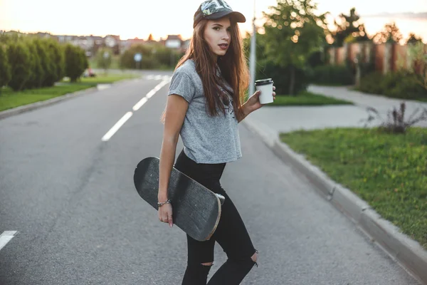 Skater girl with coffee cup in front of the sun starts her day. — Stock Photo, Image