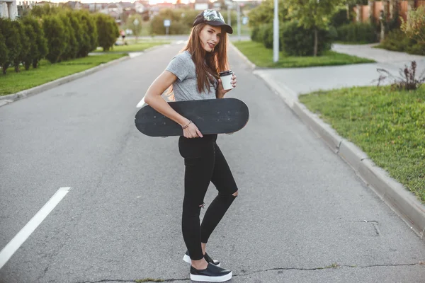 Skater girl with coffee cup in front of the sun starts her day. — Stock Photo, Image