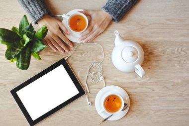 Tablo ve içecek yeşil çay oturan kız. Tablet boşluk kulaklık ile yakındaki yatıyor. Üstten Görünüm