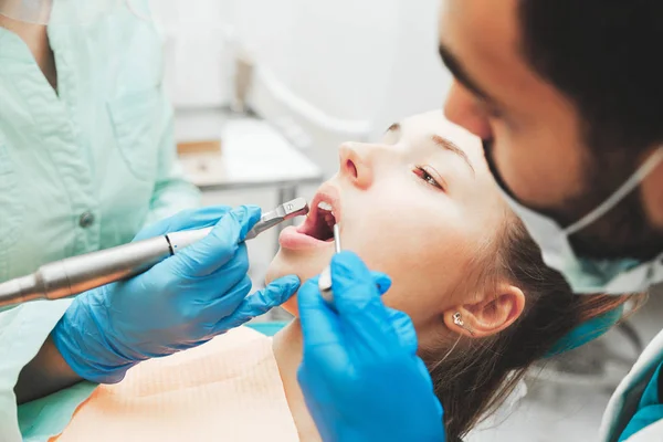 Dentists using dental drill and sucker while examining girl's mouth in clinic. — Stock Photo, Image