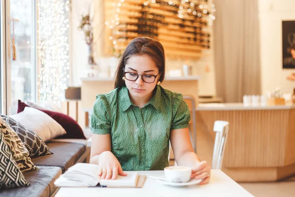 Hermosa joven mujer relajándose y leyendo un libro en la cafetería —  Fotos de Stock