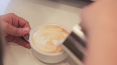 Bir barista kahve fincan haşlanmış süt ekleyerek closeup