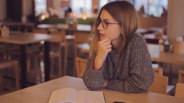 Joven hermosa mujer sueña en lugar de escribir diario, libro o notas en la cafetería — Vídeo de stock