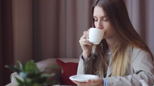 Krásná mladá dívka dělá několika doušky čaje a usmívá se, dívala se z okna — Stock video