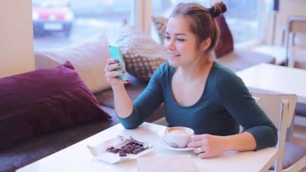 Chica en un café hablando en el chat de vídeo y viendo videos divertidos en su teléfono inteligente . — Vídeos de Stock