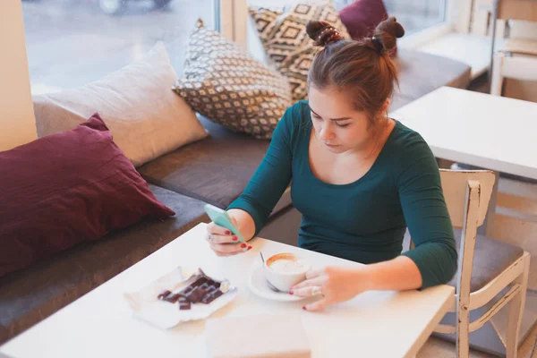 Mujer joven leyendo las noticias de la mañana de las redes sociales en el teléfono inteligente sentado en la cafetería —  Fotos de Stock