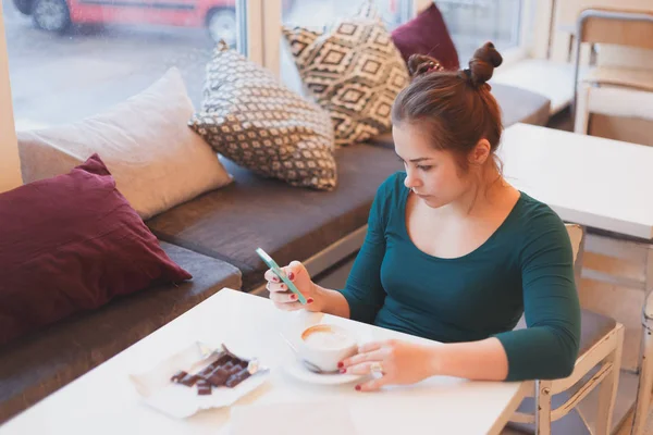 Mujer joven leyendo las noticias del mundo de la mañana en el teléfono inteligente sentado en la cafetería —  Fotos de Stock