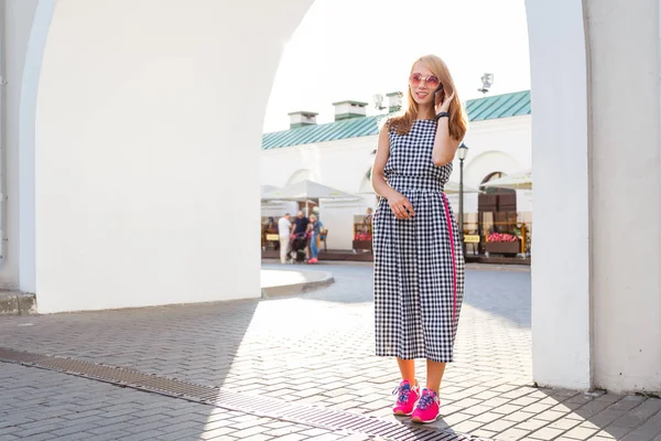 세로 거리에 걷는 유행 금발 여자. 그녀는 전화를 말하기. — 스톡 사진