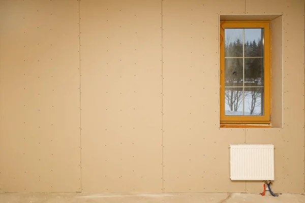 Calefacción radiador debajo de la ventana en la habitación sin terminar durante la construcción. Copiar espacio en la parte izquierda — Foto de Stock