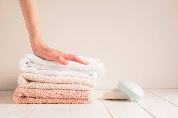 Mano de mujer y una pila de toallas suaves con jabón en una mesa rústica. El concepto de una piel sana de las manos — Foto de Stock