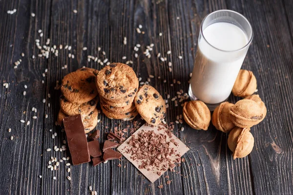Chocolate and nut shaped Cookies, crushed chocolate with glass of Milk on a dark wooden table
