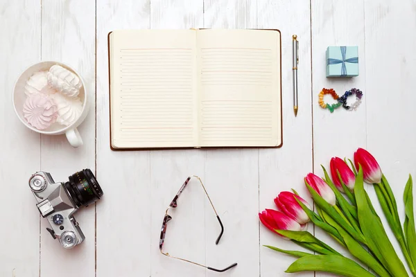 Inspirerende bureaublad van meisjes werken als schrijver. Geopende dagboek en pen, vintage camera, een boeket van rode tulpen en marshmallows in de Witte mok. Bovenaanzicht — Stockfoto