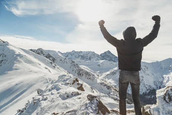 Happy man raising hands on top of snowy mountains.