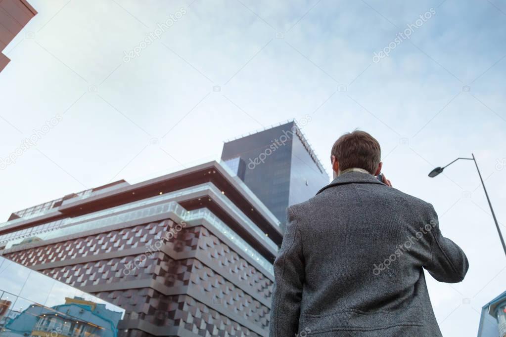 A young man in a coat makes an anonymous phone call standing near the business center.