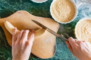 Kadın bir muz kaba ahşap tahta üzerinde bir bıçakla keser. Üstten Görünüm.