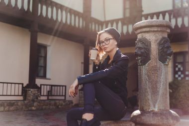 Siyah örme şapka ve gözlük fincan kahve bahçesinde oturan genç kadın.