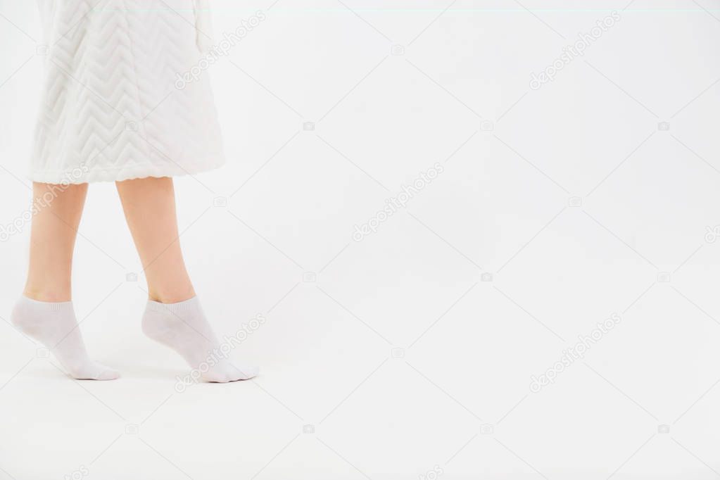 A girl in a white bathrobe and socks goes on socks after a shower. Close-up of beautiful female slender legs. Side view.