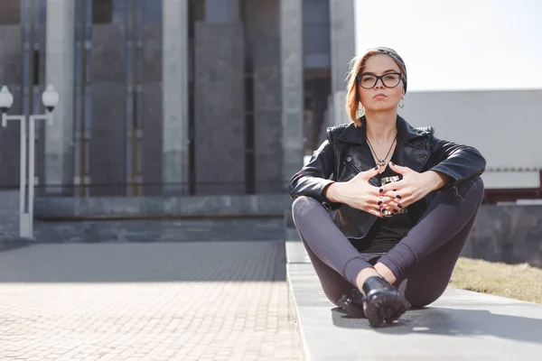 Concepto de moda de calle - chica cool con estilo de rock negro sentado entre el fondo urbano al aire libre —  Fotos de Stock