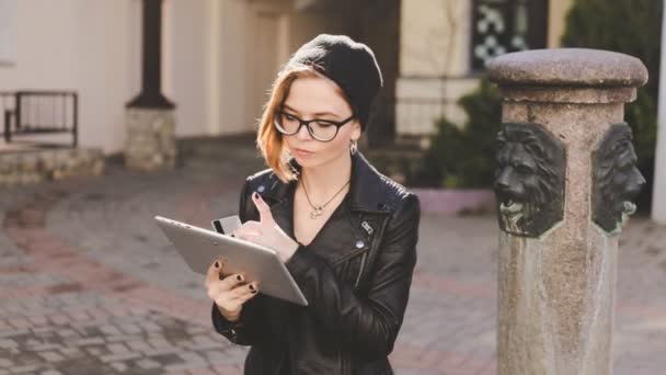 Moderne stijlvolle meisje betaalt de bestelling via Internet. Maakt gebruik van een bankkaart en tablet zitten in de tuin op de straat. — Stockvideo