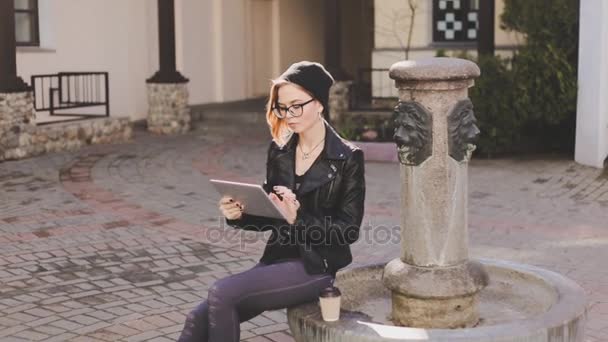 Young fashionably dressed woman looks through the messages on social networks on her tablet and expressively laughs — Stock Video