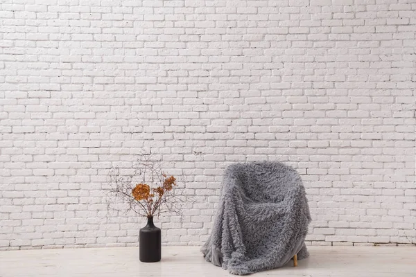 Interior in the style of minimalism. Chair and pot with dry branches against a white brick wall.
