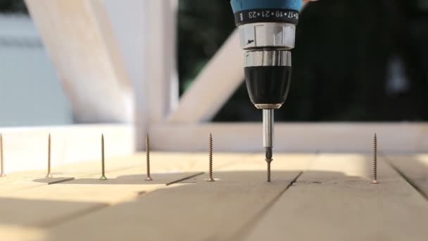 De man draait de schroeven in de planken met behulp van een schroevendraaier. — Stockvideo