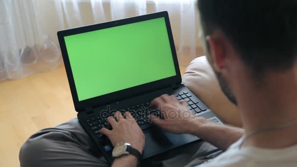 L'uomo tira su un computer portatile seduto su una poltrona. Schermo verde per il contenuto dello schermo personalizzato . — Video Stock