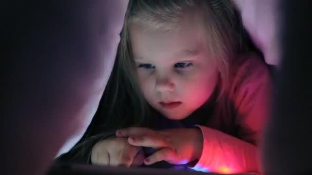 Carino bambina sdraiata sotto coperta con tablet computer — Video Stock