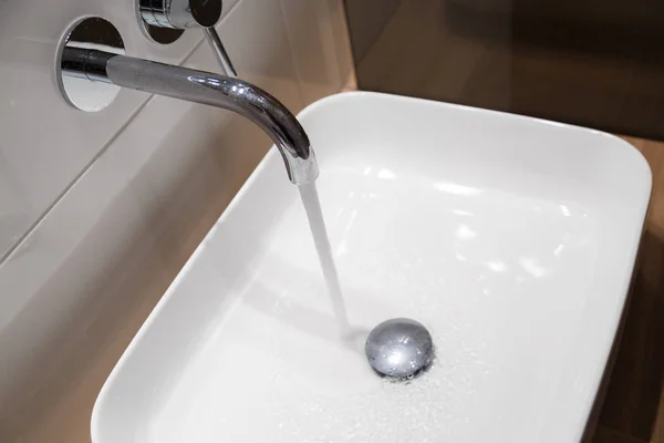 Close up of sink and faucet on wooden shelf in white bathroom interior — Stock Photo, Image