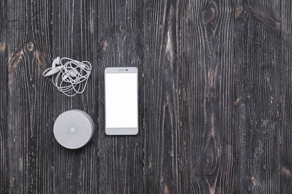 Portative sound system with earphones and mobile phone  blank screen on dark wooden table