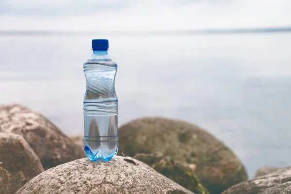 Pequeña botella de agua en la piedra del océano en el fondo natural — Foto de Stock