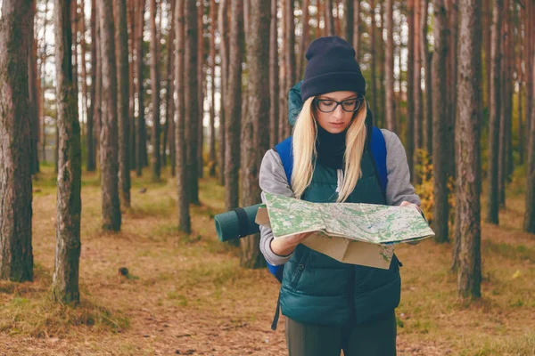 一个美丽的年轻女子在松树林的旅行地图和背包 — 图库照片