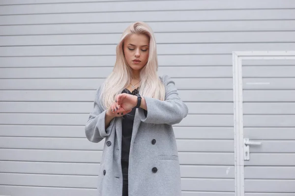 Porträtt av unga blondhair elegant klädd kvinna i en kappa använder en smart armband som står utomhus — Stockfoto