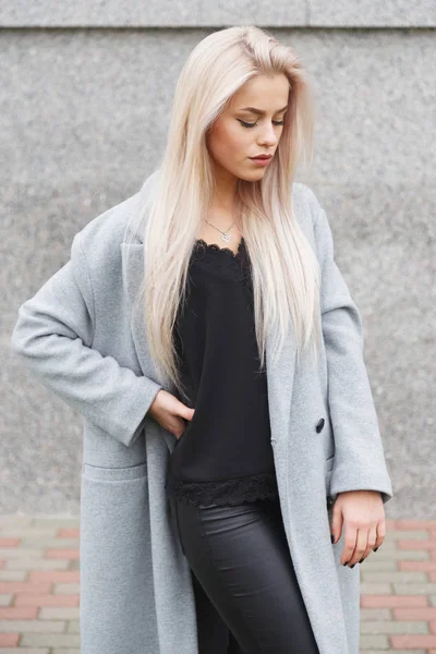 Портрет красивой молодой блондинки в сером пальто и черных кожаных штанах. Уличная мода — стоковое фото