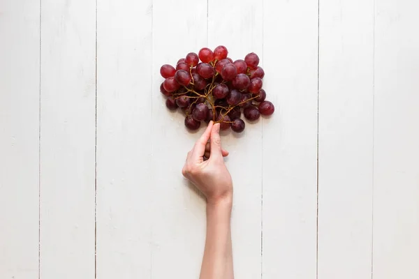 La main des filles s'accroche à un bouquet de raisins rouges sur un fond en bois. Vue d'en haut. Les raisins sont comme des ballons . — Photo