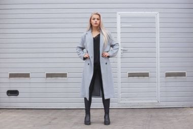 Kaba sokak duvara, minimalist kentsel giyim tarzı poz gri ceket giyen zarif genç kadın