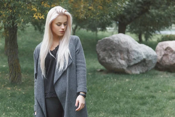 Portræt af ung blondhår elegant klædt kvinde i en frakke med smart armbånd stående udendørs . - Stock-foto